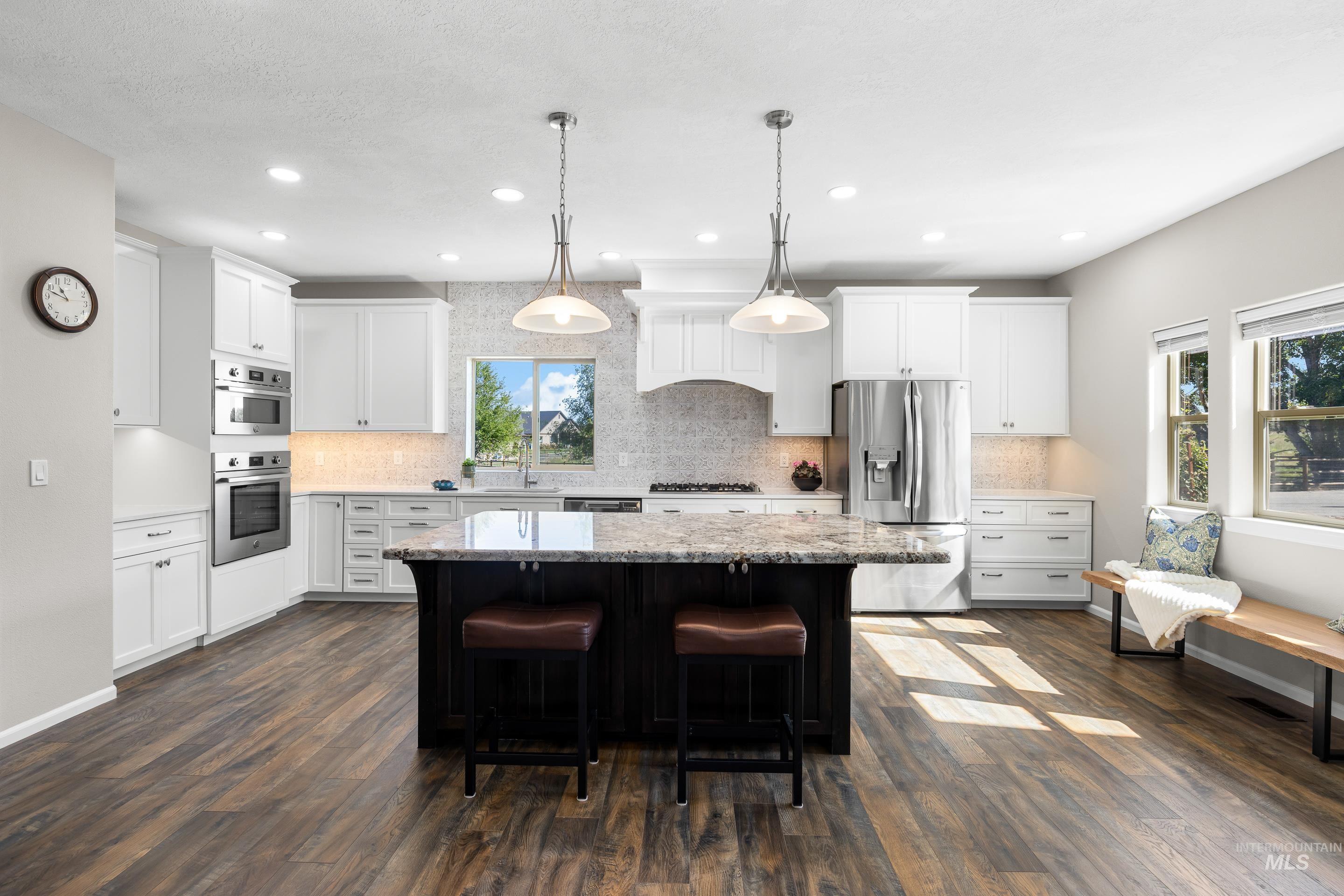 14119 Silver Ridge Road Caldwell, ID 83607 - Photo 15 of 50 Kitchen featuring white cabinetry, hanging light fixtures, light stone counters, appliances with stainless steel finishes, and dark wood-style floors