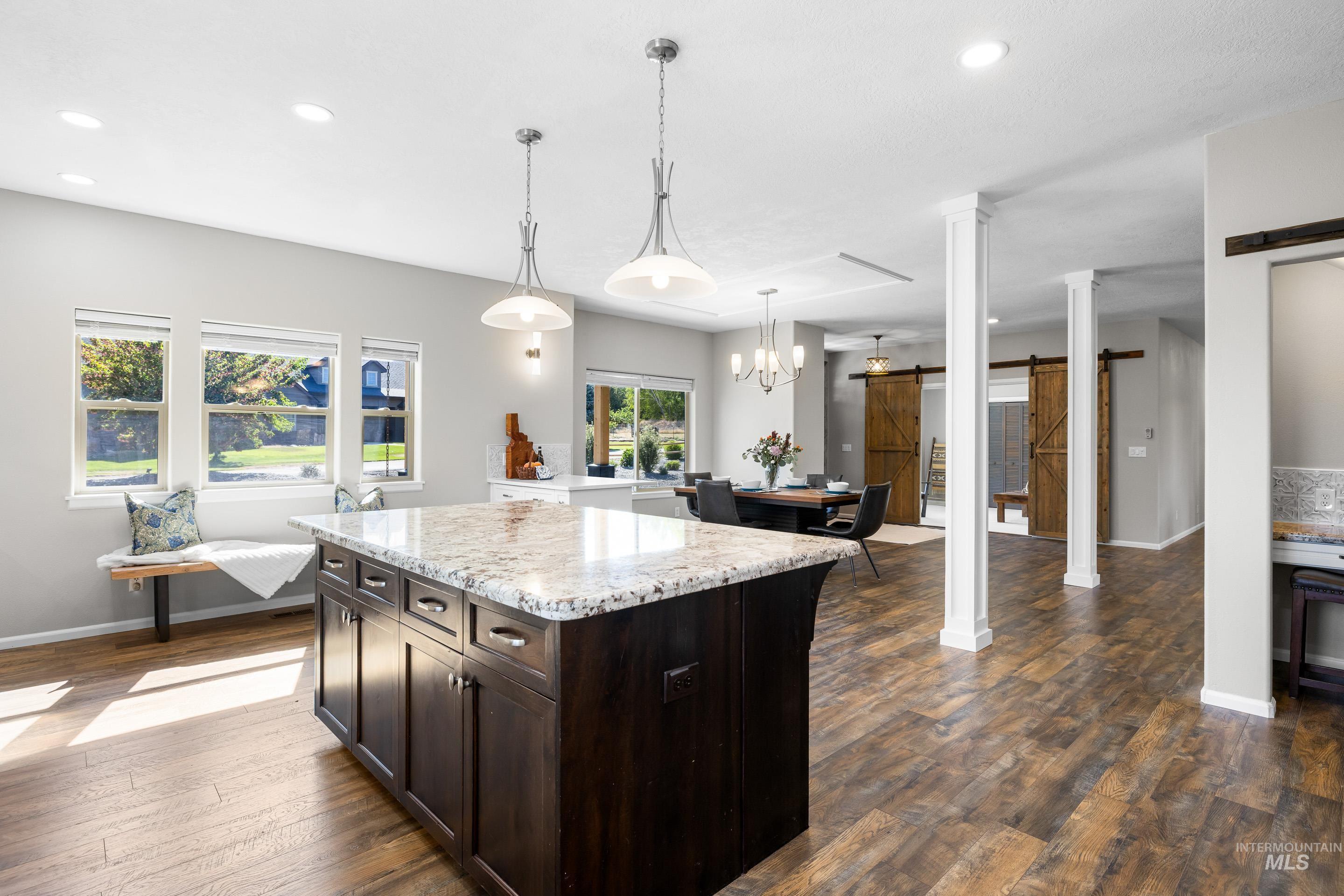 14119 Silver Ridge Road Caldwell, ID 83607 - Photo 17 of 50 Kitchen featuring a barn door, dark brown cabinets, light stone counters, decorative light fixtures, and dark wood-type flooring