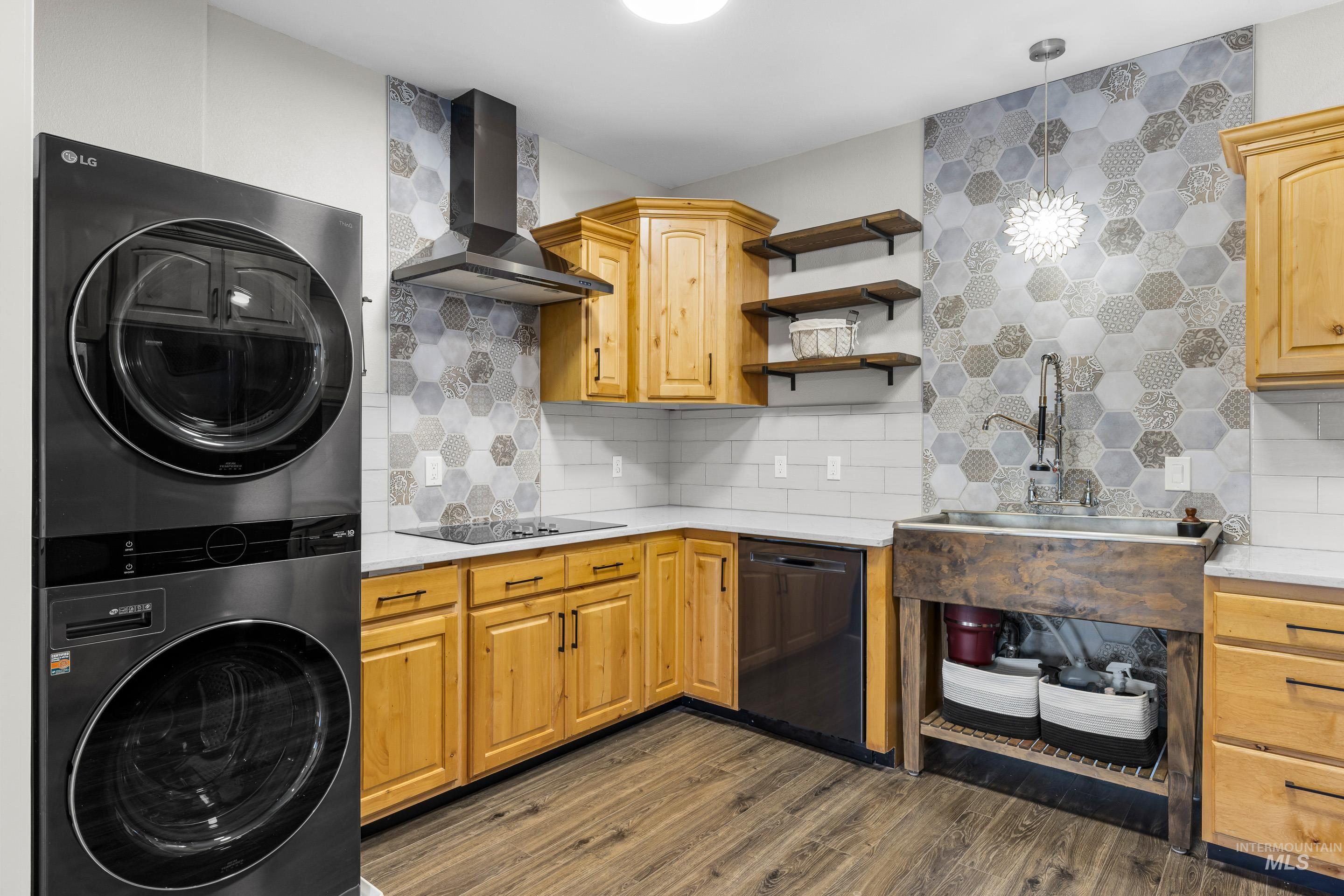 14119 Silver Ridge Road Caldwell, ID 83607 - Photo 31 of 50 Kitchen featuring decorative backsplash, wall chimney exhaust hood, dark wood-type flooring, stacked washing machine and dryer, and black dishwasher