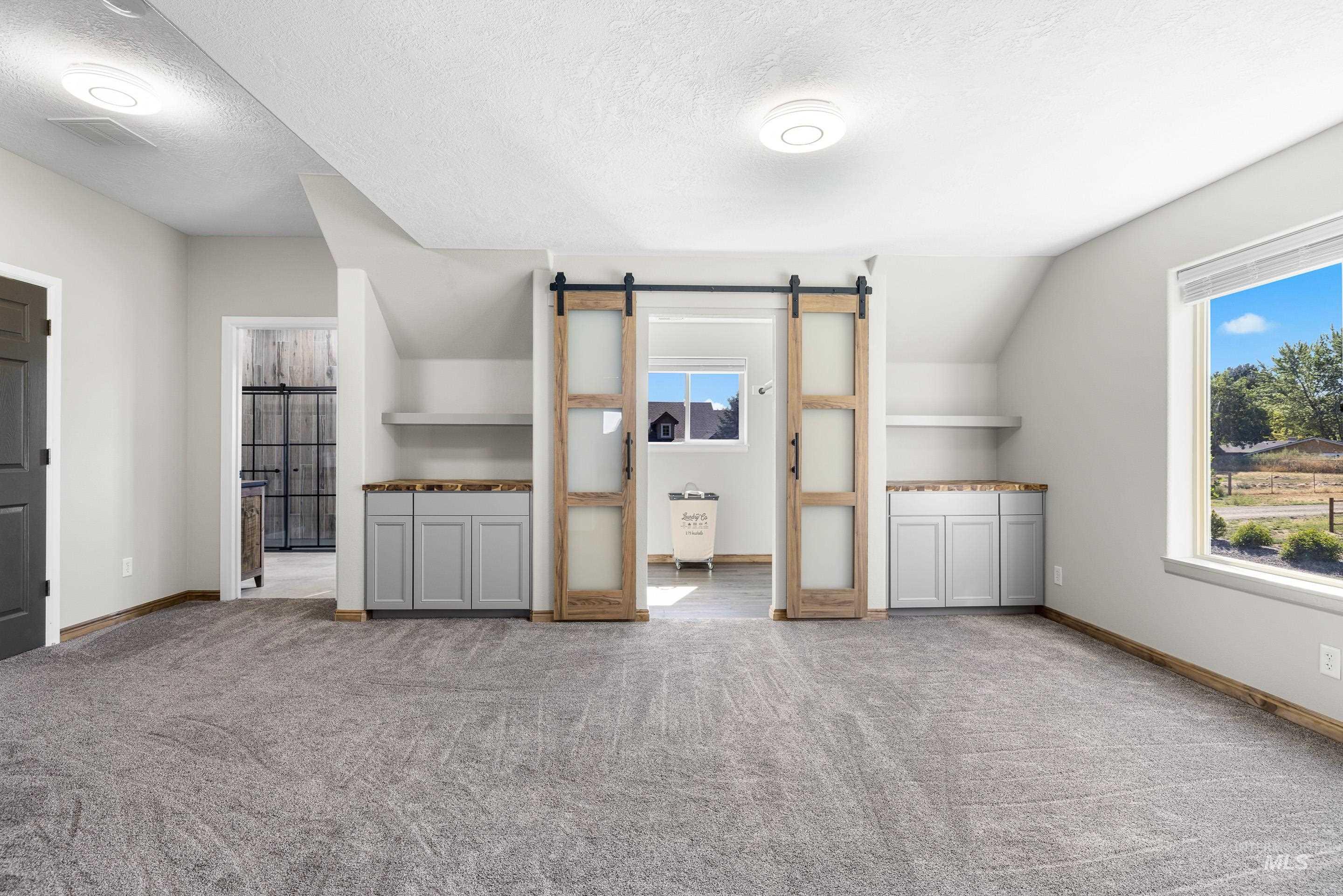 14119 Silver Ridge Road Caldwell, ID 83607 - Photo 39 of 50 Additional living space featuring a barn door, a textured ceiling, light carpet, and vaulted ceiling