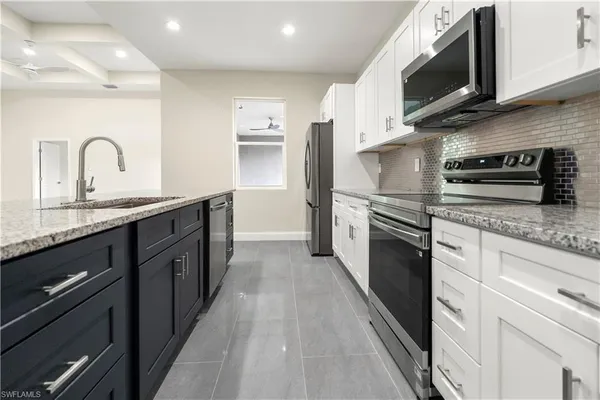 a large kitchen with stainless steel appliances granite countertop a stove a sink dishwasher and a microwave oven with white cabinets