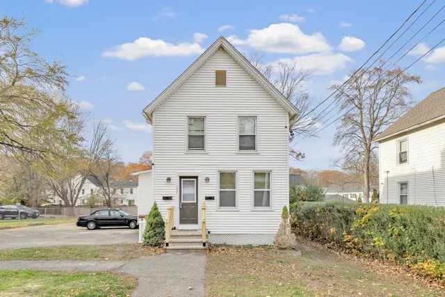 a view of a white house next to a yard with big trees