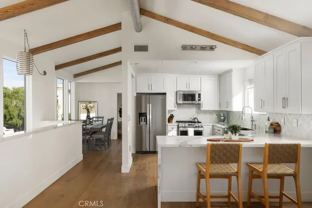 a kitchen with stainless steel appliances kitchen island granite countertop a refrigerator a stove a sink a dining table and chairs with wooden floor