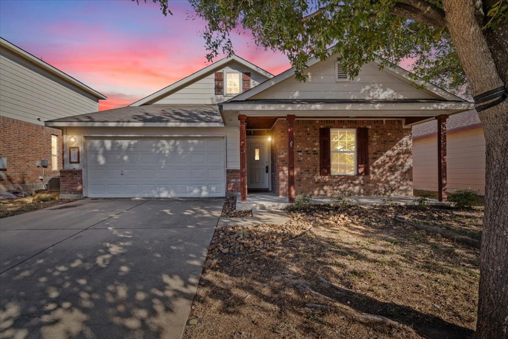 Traditional-style house featuring driveway, brick siding, a porch, and a garage