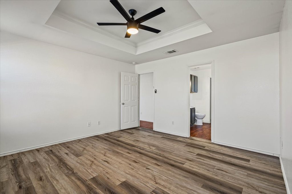 17912 Aleppo Pine Elgin, TX 78621 - Photo 14 of 30 Unfurnished bedroom with a ceiling fan, a tray ceiling, wood finished floors, ornamental molding, and ensuite bath
