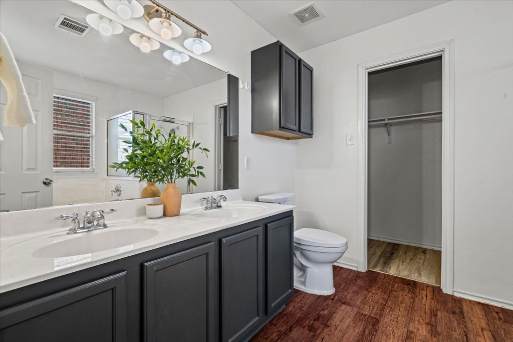 17912 Aleppo Pine Elgin, TX 78621 - Photo 15 of 30 Bathroom with double vanity, dark wood-style floors, a spacious closet, and a shower stall