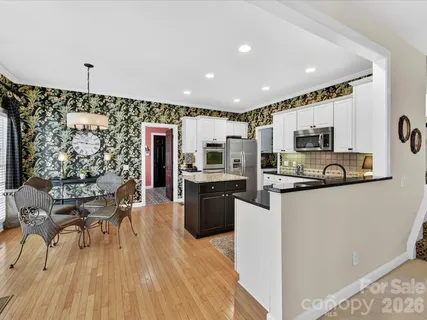 a kitchen with stainless steel appliances granite countertop a refrigerator a stove top oven a sink dishwasher and white cabinets with wooden floor