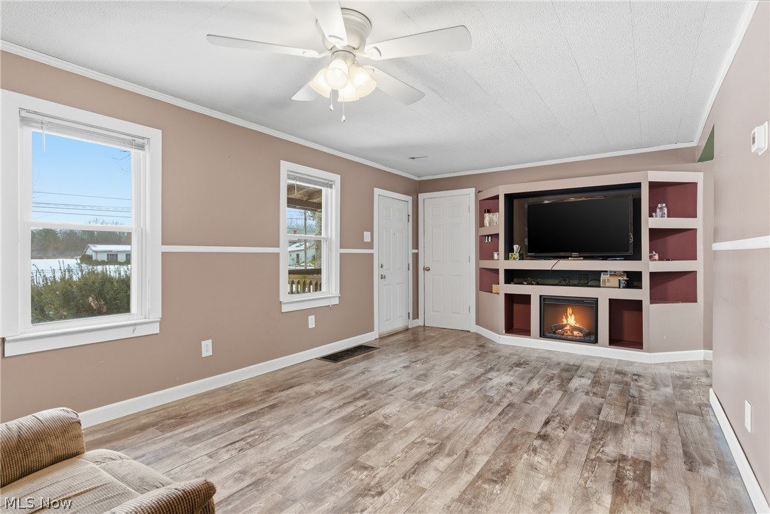 6291 Downs Road Northwest Warren, OH 44481 - Photo 11 of 44 Unfurnished living room with ceiling fan, light wood-style flooring, ornamental molding, and a lit fireplace