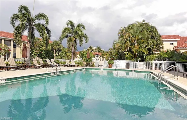 a view of a swimming pool with a lawn chairs under palm trees