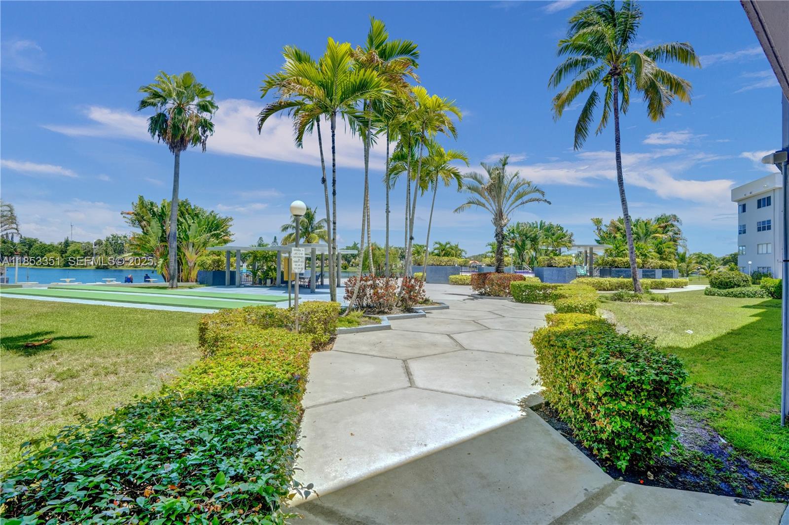 873 Northeast 195th Street, Unit 309 North Miami Beach, FL 33179 - Photo 32 of 35 a view of a swimming pool with a garden and palm trees