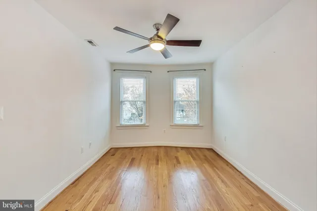 an empty room with wooden floor windows and fan