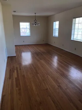 an empty room with wooden floor chandelier and windows