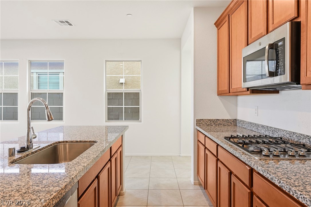 250 Dedication Avenue Henderson, NV 89011 - Photo 14 of 67 Kitchen with wood finish cabinets, stainless steel appliances, light tile patterned flooring, light stone counters, and plenty of natural light