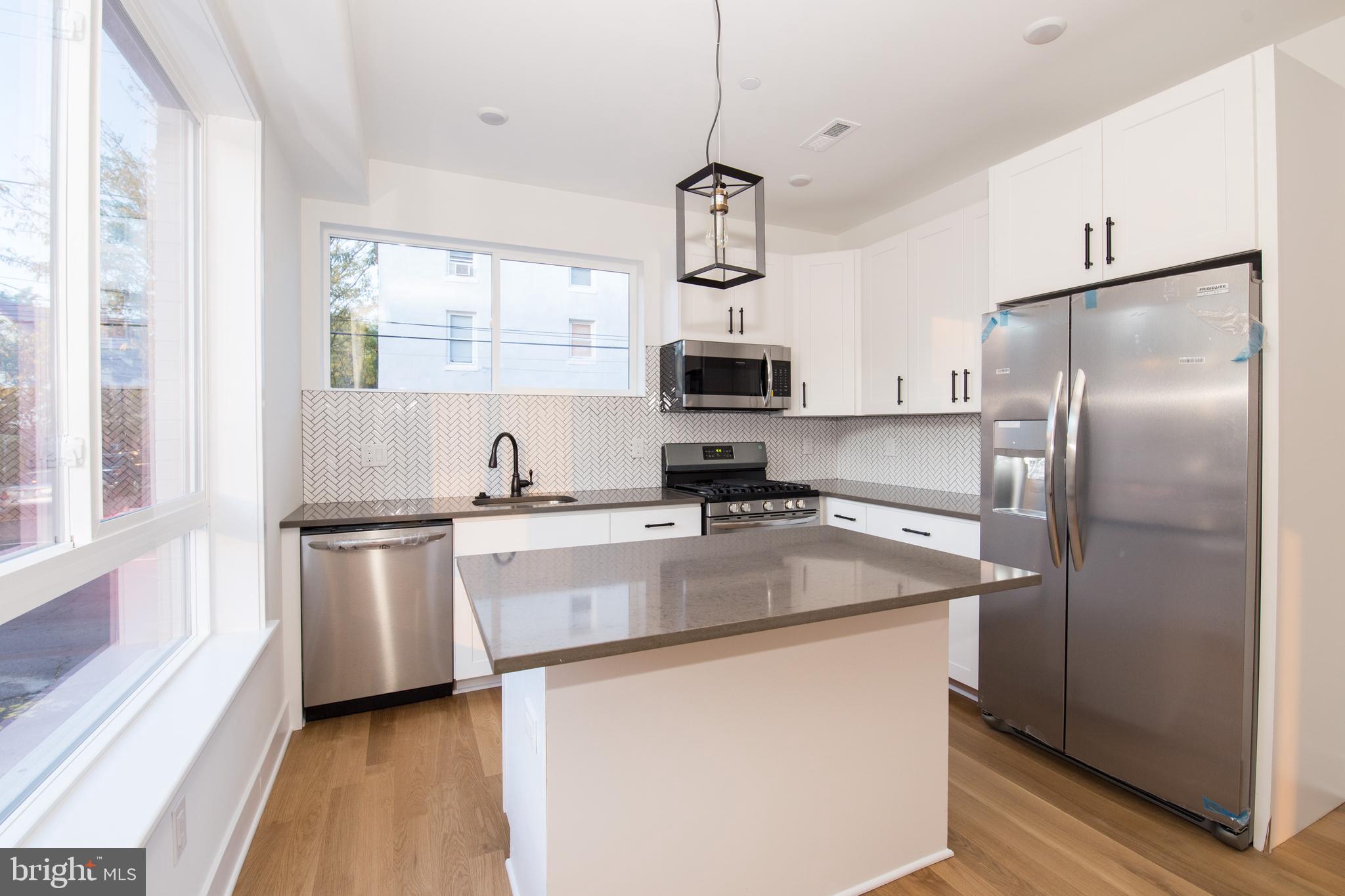 a kitchen with stainless steel appliances granite countertop a refrigerator a sink dishwasher a stove top oven a refrigerator and white cabinets with wooden floor