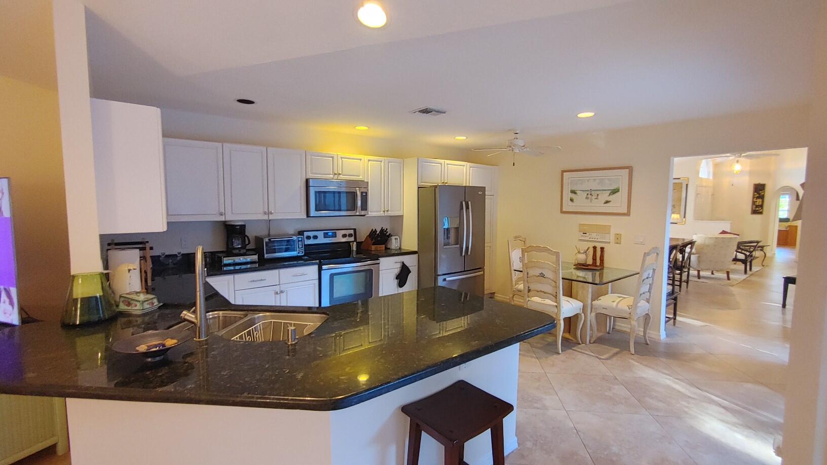 16461 Riverwind Drive Jupiter, FL 33477 - Photo 11 of 45 a living room with stainless steel appliances kitchen island granite countertop a table chairs and a refrigerator