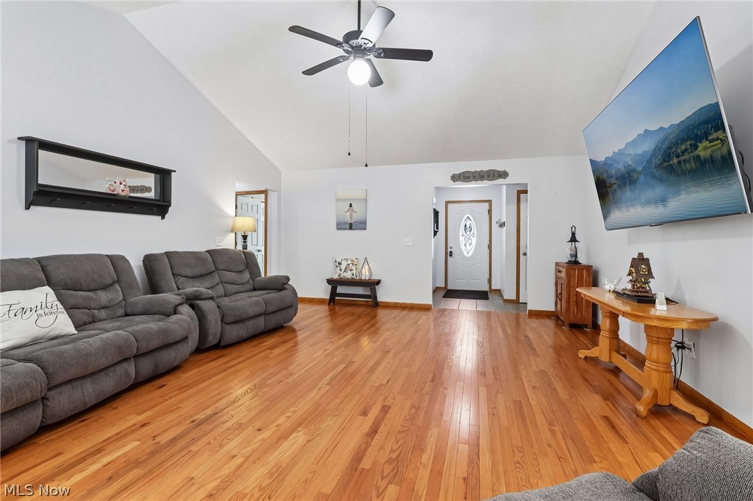 3213 Bates Road Madison, OH 44057 - Photo 9 of 45 Spacious living area featuring high vaulted ceilings, polished wood flooring, a ceiling fan with integrated lighting, recessed wall space, and a white front entry door with decorative glass