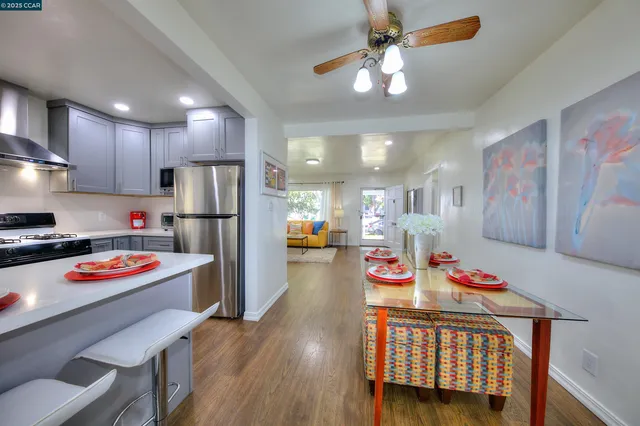 a open kitchen with stainless steel appliances granite countertop a refrigerator a stove top oven a island and couches with wooden floor