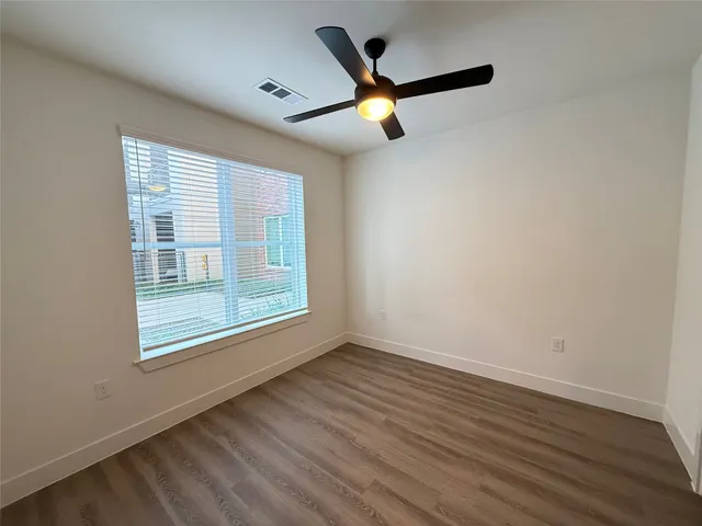 an empty room with wooden floor fan and windows