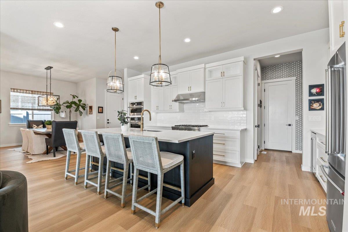 Kitchen with decorative light fixtures, white cabinetry, backsplash, an island with sink, and a breakfast bar
