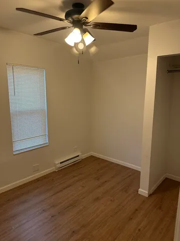 an empty room with wooden floor fan and windows