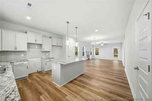 a large kitchen with kitchen island a stove a sink dishwasher a refrigerator white cabinets and wooden floor next to a window