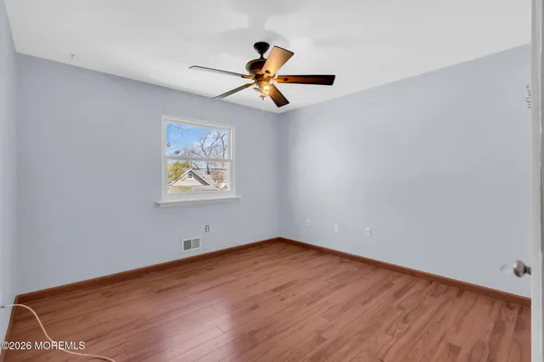 an empty room with wooden floor ceiling fan and windows