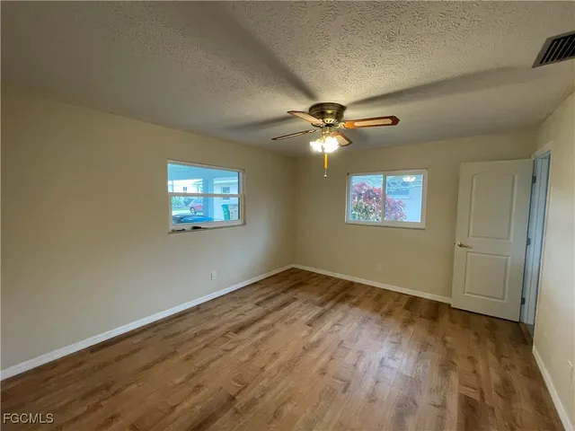 an empty room with wooden floor chandelier fan and windows