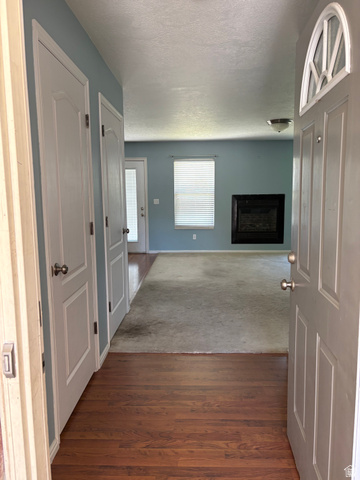 587 West 2400 South Perry, UT 84302 - Photo 11 of 46 Entryway featuring wood-finish flooring, leading to a living area with light blue walls, a fireplace with a dark surround, and a window with blinds