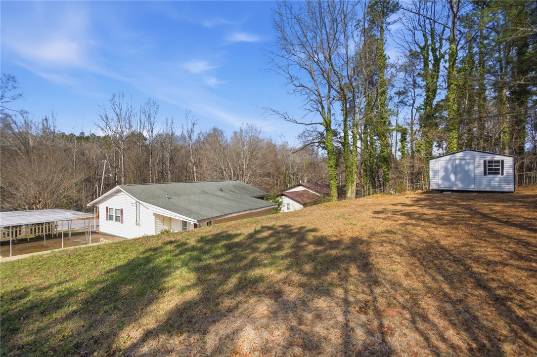 108 Hodge Street Abbeville, SC 29620 - Photo 27 of 39 A quaint white residence with a long, inviting driveway is nestled in a clearing, surrounded by a serene, natural wooded landscape.