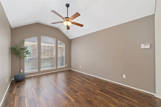 an empty room with wooden floor fan and windows