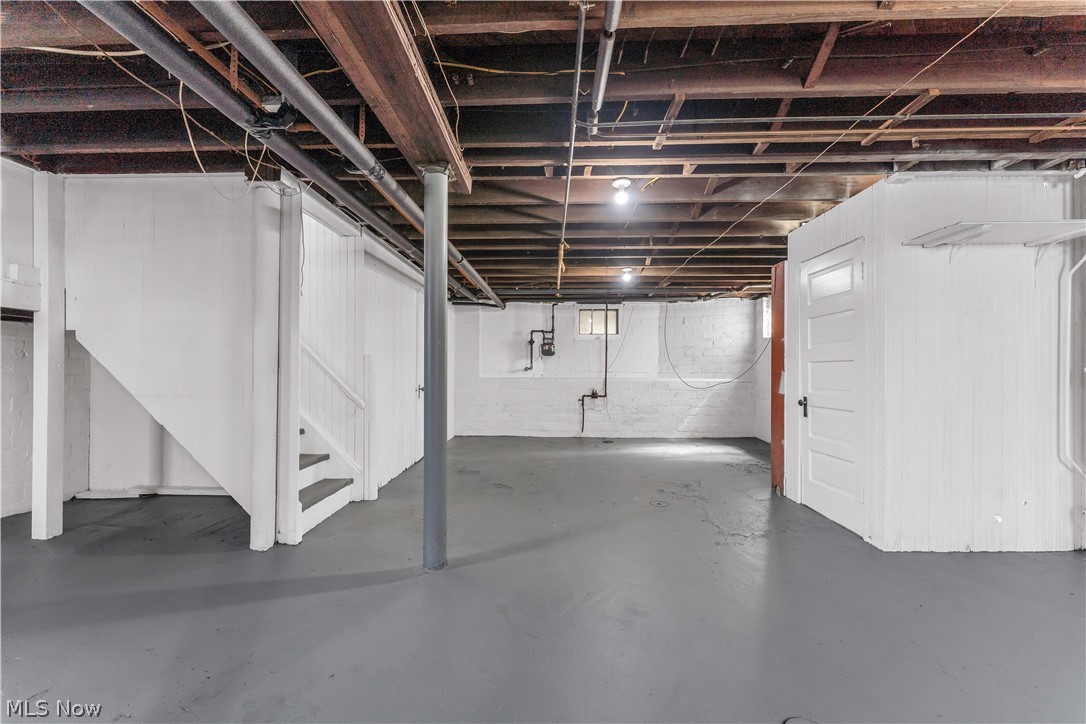 3506 Riverside Avenue Cleveland, OH 44109 - Photo 25 of 31 Spacious unfinished basement featuring a grey painted concrete floor, exposed wood ceiling joists, white painted block walls, and a white painted stairway with wood treads and risers