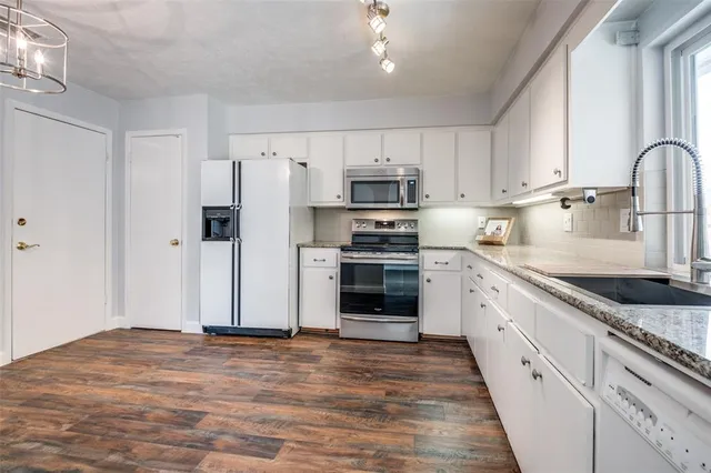 a kitchen with granite countertop a refrigerator oven a sink dishwasher and white cabinets with wooden floor