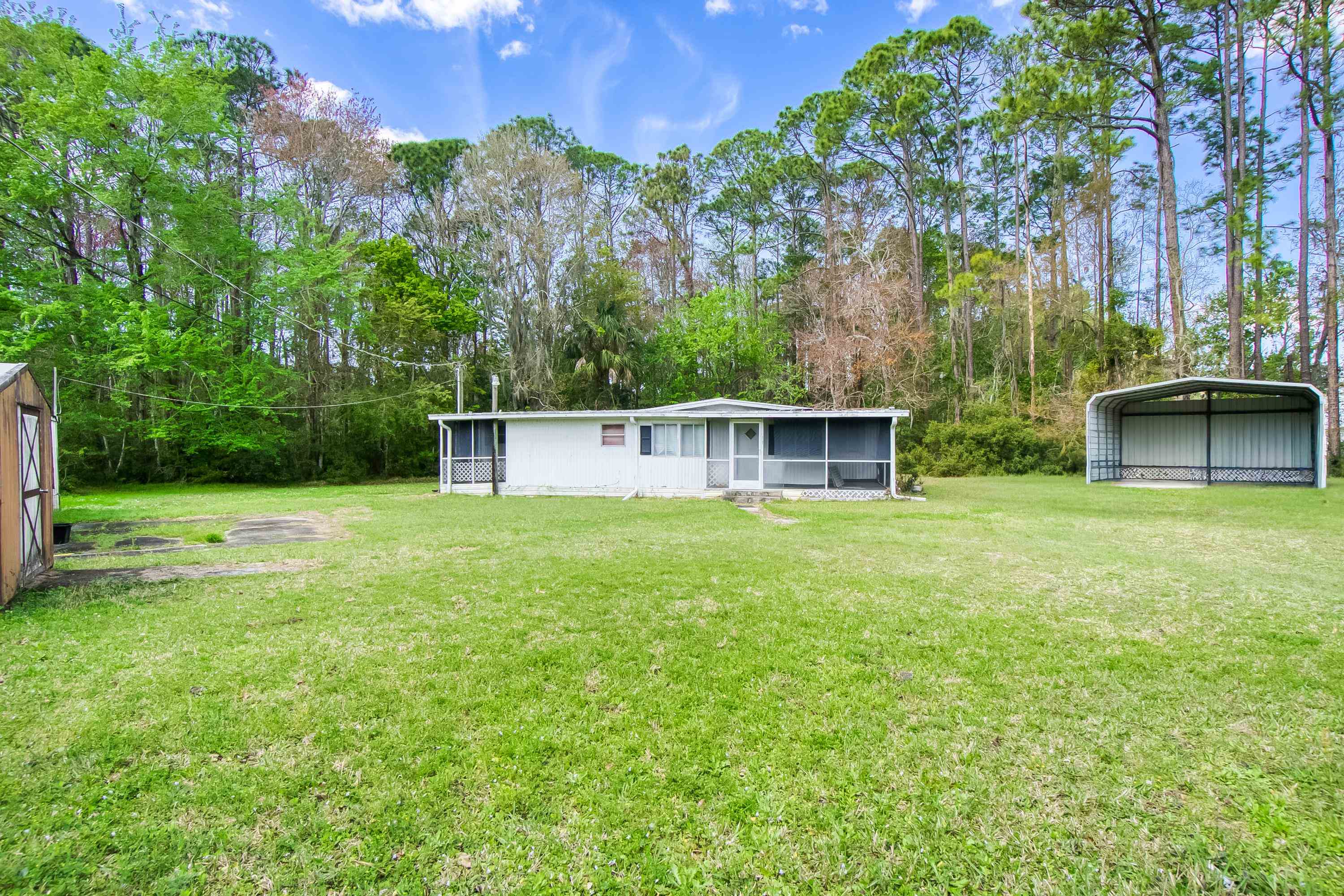2785 Stratton Boulevard St. Augustine, FL 32084 - Photo 9 of 25 Back of house with a detached carport, a yard, a sunroom, view of wooded area, and an outdoor structure