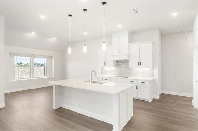 a kitchen with a sink a stove a wooden floor and white cabinets