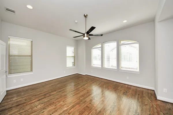 an empty room with wooden floor a ceiling fan and windows
