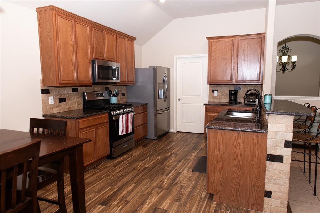 5125 Shelly Ray Road Fort Worth, TX 76244 - Photo 8 of 27 Kitchen featuring a breakfast bar area, backsplash, stainless steel appliances, dark stone counters, and vaulted ceiling