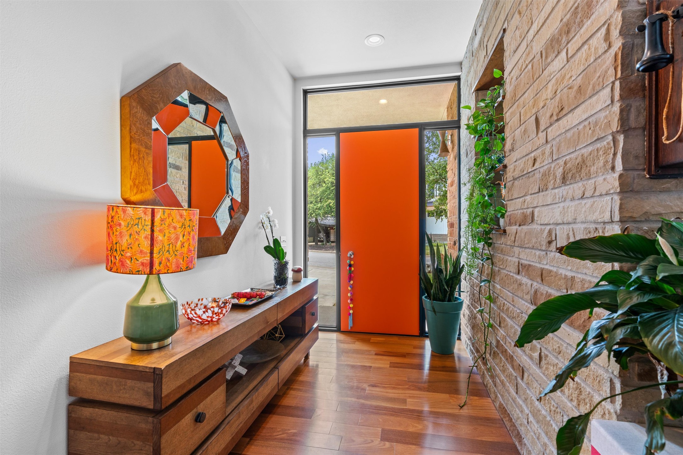 408 Starlight Village Loop Leander, TX 78641 - Photo 3 of 40 A vibrant orange door welcomes guests into a naturally illuminated entry, complemented by rich hardwood flooring and a textured stone wall.
