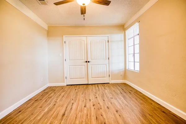 an empty room with wooden floor chandelier fan and windows