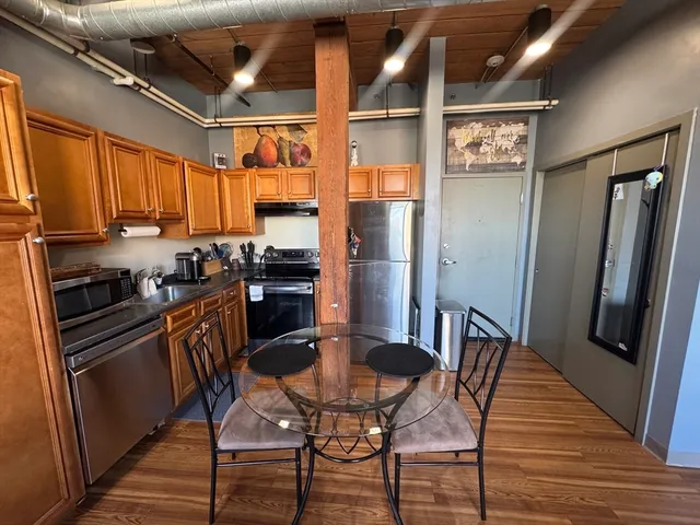 a kitchen with stainless steel appliances granite countertop a refrigerator a stove a sink dishwasher and a dining table with wooden floor