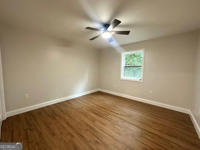 an empty room with wooden floor fan and windows