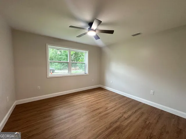 an empty room with wooden floor ceiling fan and windows