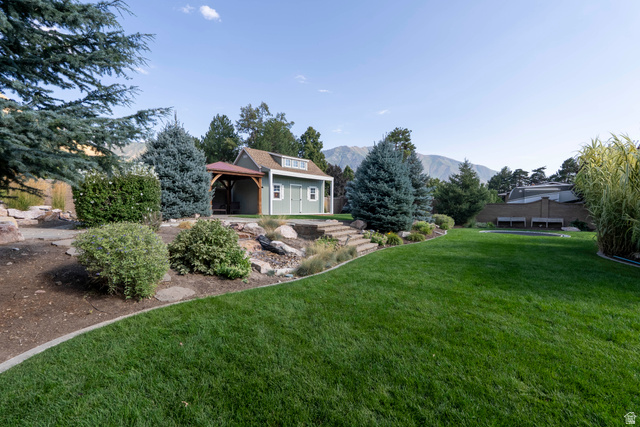 687 South 2080th Street East Springville, UT 84663 - Photo 97 of 149 Expansive backyard featuring a large green lawn, mature trees, and a terraced landscape leading to a detached shed with an attached covered patio