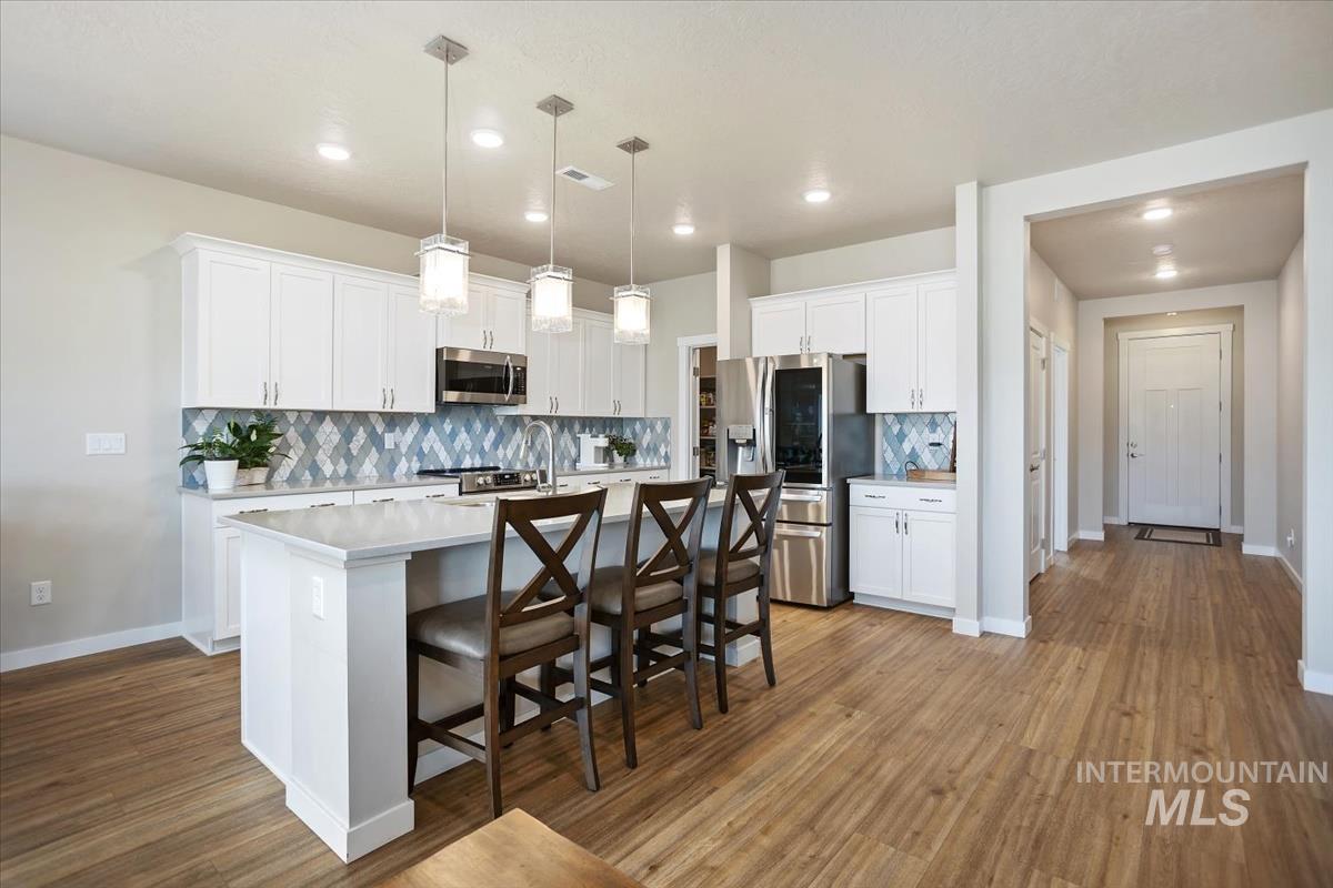 3729 South Maple Ridge Avenue Nampa, ID 83686 - Photo 12 of 46 Kitchen with a breakfast bar area, a center island with sink, white cabinetry, decorative backsplash, and stainless steel appliances