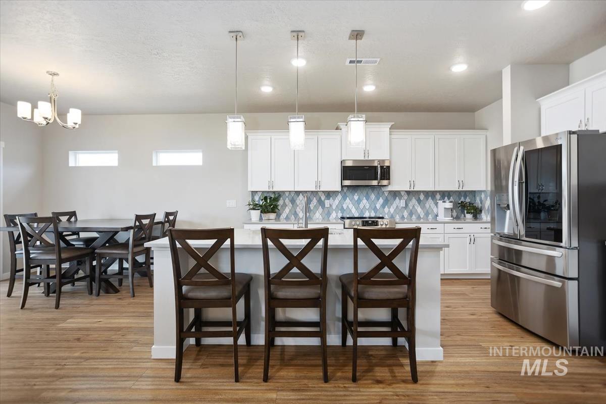 3729 South Maple Ridge Avenue Nampa, ID 83686 - Photo 13 of 46 Kitchen with stainless steel appliances, a center island with sink, a breakfast bar, tasteful backsplash, and light wood-style floors