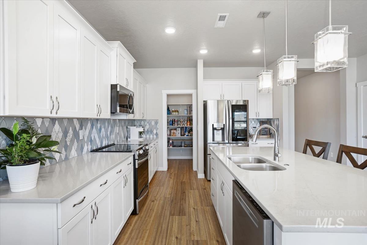 3729 South Maple Ridge Avenue Nampa, ID 83686 - Photo 14 of 46 Kitchen with an island with sink, stainless steel appliances, a kitchen bar, white cabinetry, and light stone counters