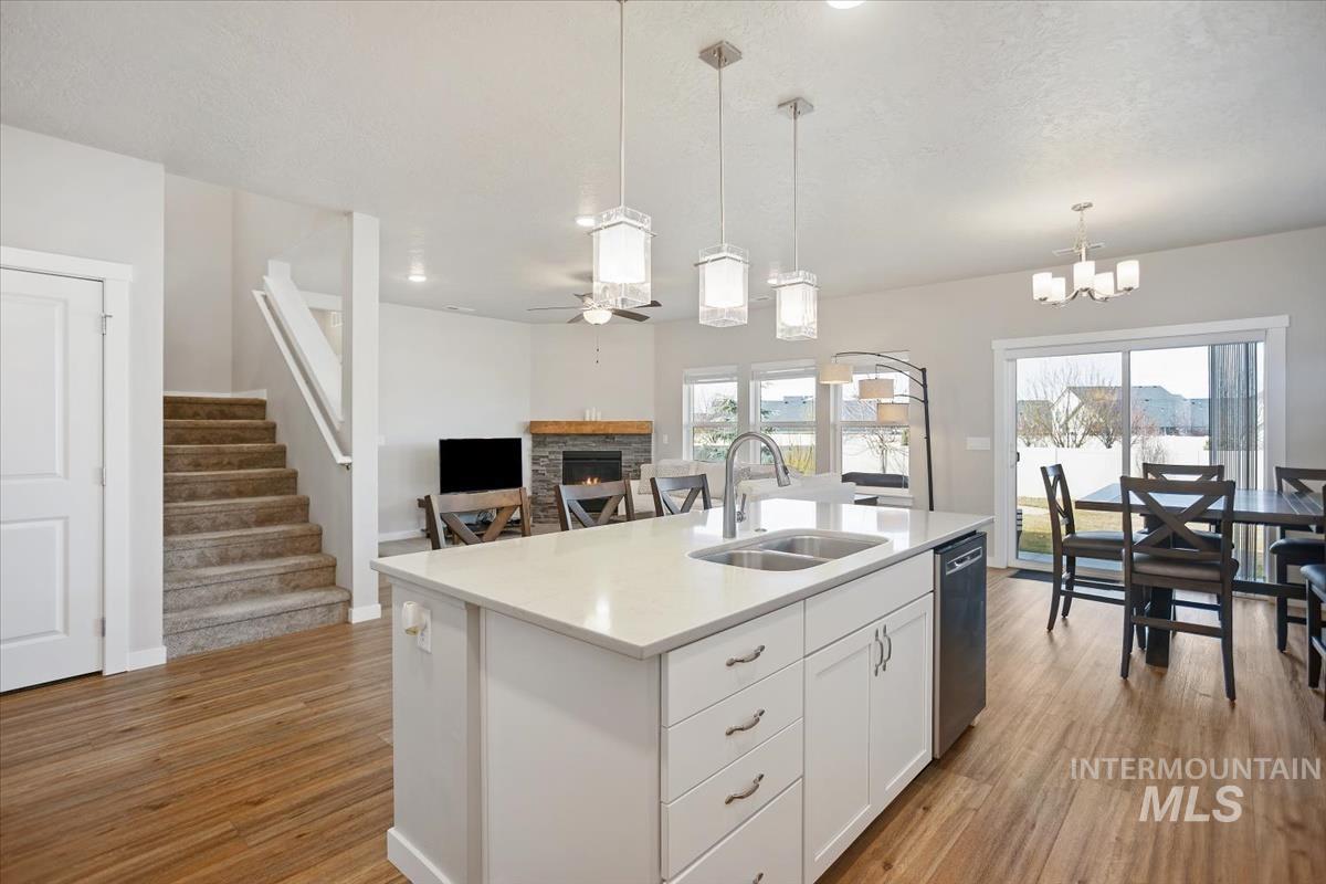 3729 South Maple Ridge Avenue Nampa, ID 83686 - Photo 46 of 46 Kitchen featuring white cabinetry, an island with sink, a stone fireplace, open floor plan, and light wood-style floors