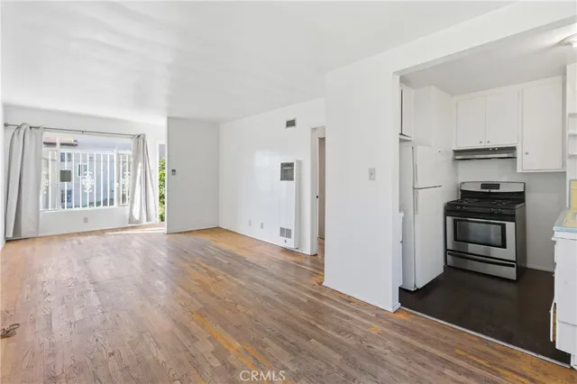 an empty room with wooden floor kitchen view and windows