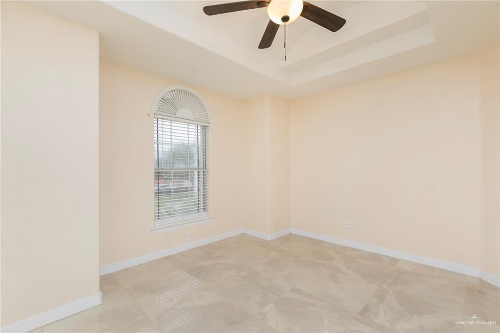 2001 Quail Lane Mission, TX 78572 - Photo 20 of 28 Room featuring a tray ceiling with a ceiling fan and light fixture, a large arched window with blinds, and light-toned tile flooring