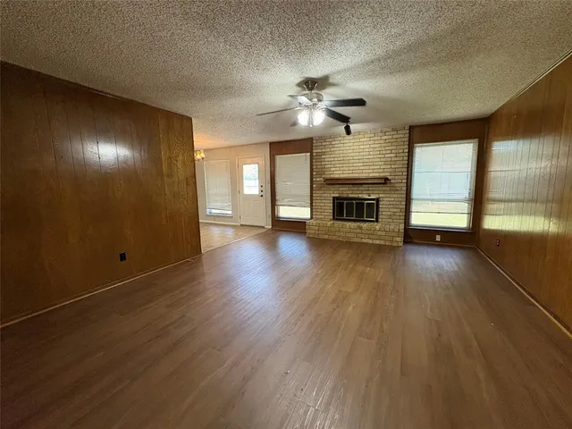 an empty room with wooden floor fireplace cabinet and windows