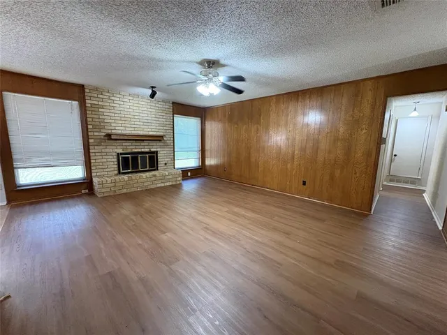 an empty room with wooden floor fireplace and windows